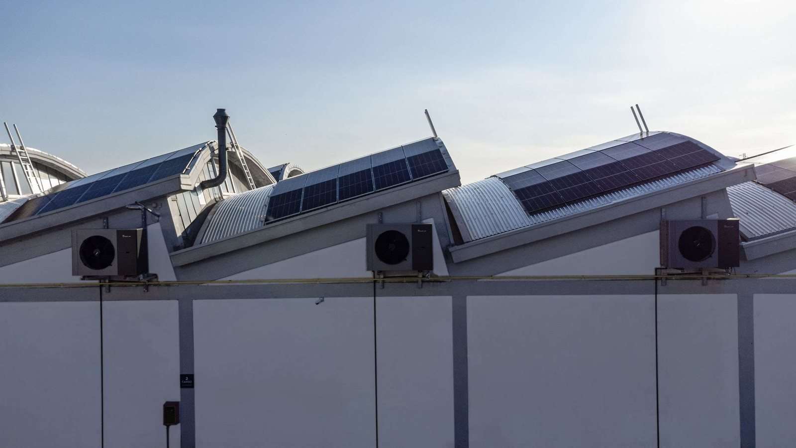 Solceller på tagene af en hal og Kita Air-udedele langs muren: strømmen produceret om dagen bruges af klimaanlægget