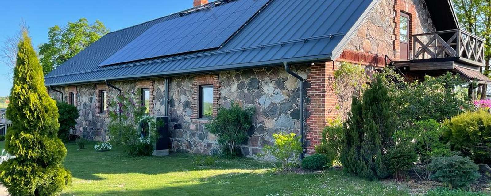 Stenhus i Letland med solceller på taget og luft til vand varmepumpe med propan ved muren