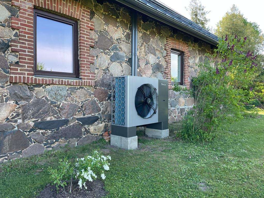 Luft/vand-varmepumpe på propan ved siden af et stenhus i Letland: forbruget afhænger af, hvor meget varme huset beder om, ikke af typeskiltet
